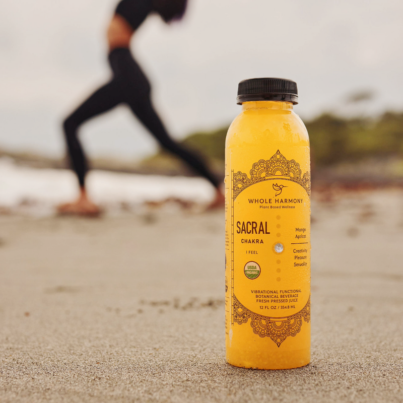 Sacral Chakra beverage from Whole Harmony on the beach in front of woman doing a yoga pose.